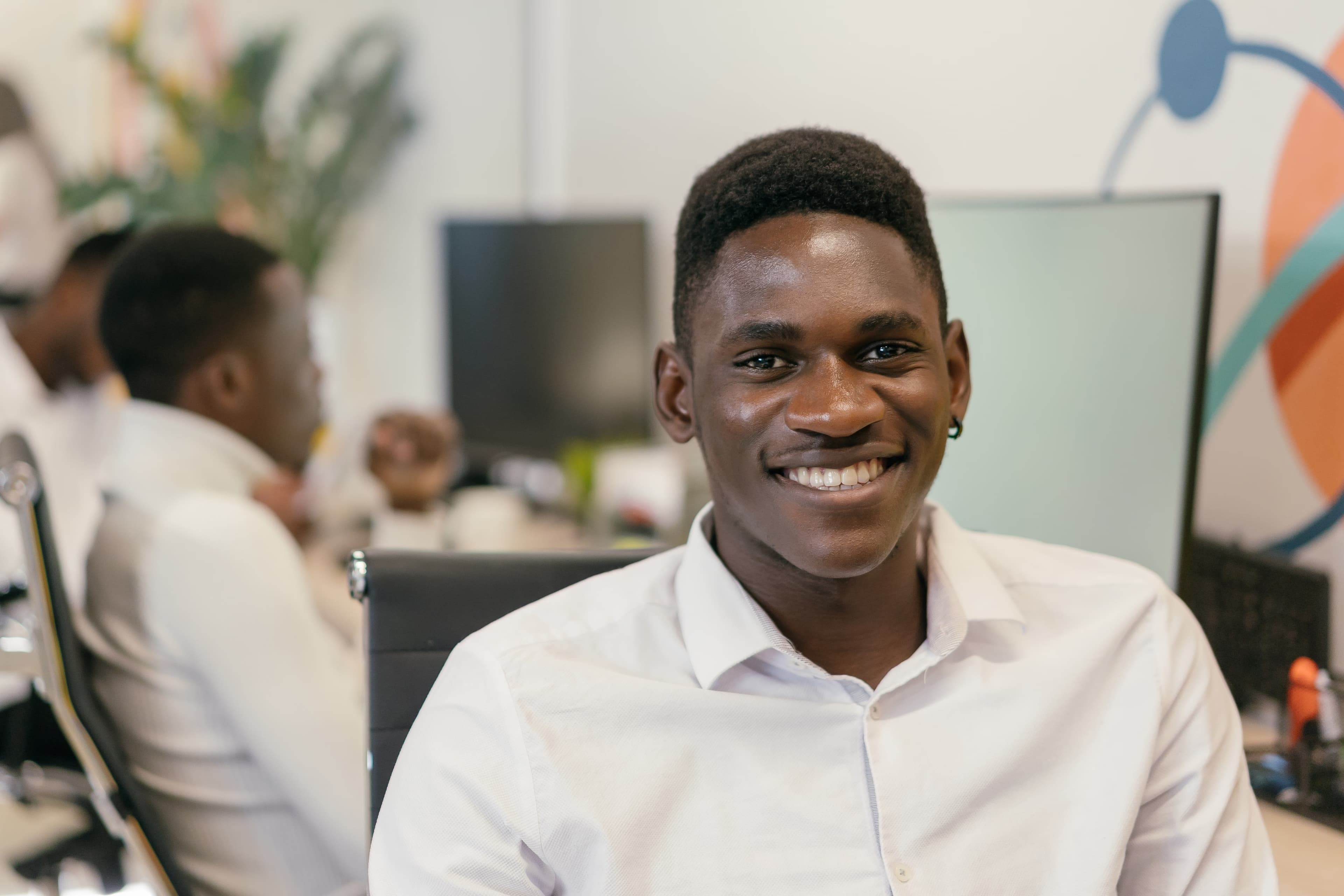 A smiling learner at a desk, colleagues working in the background